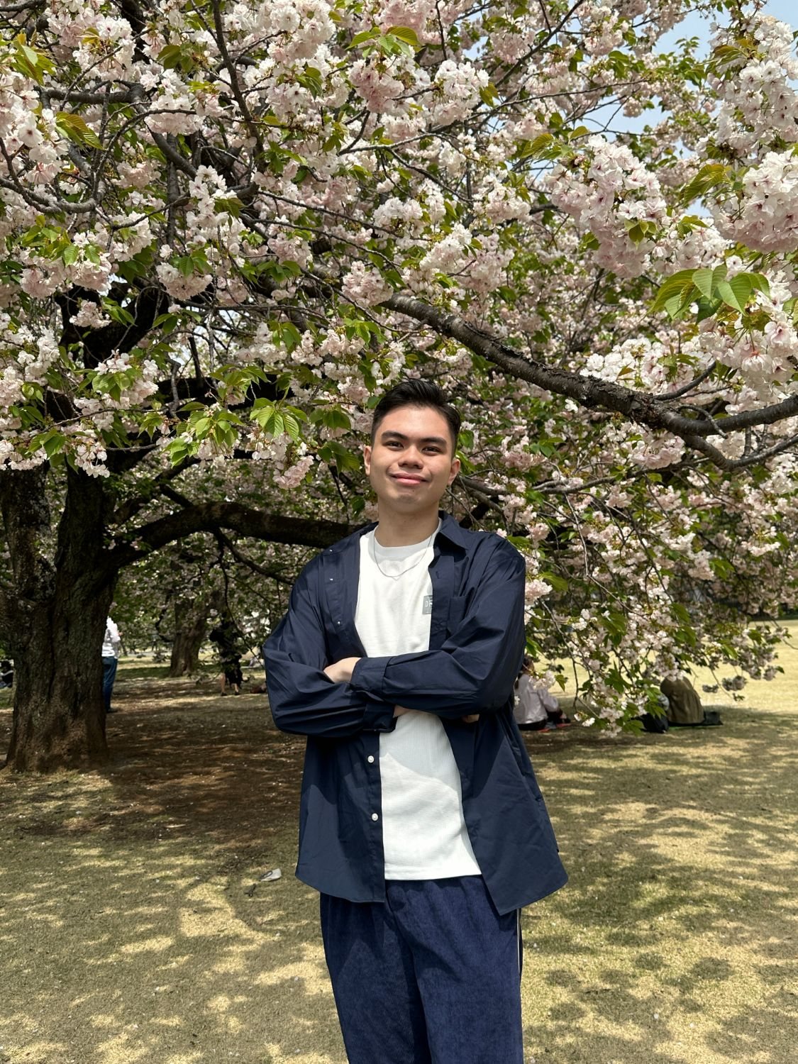 Prince Buencamino under a cherry tree in bloom, arms crossed, smiling